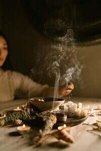 Woman seated at a table with herbs burning.