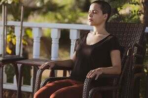 A woman sitting in a chair on a porch, deep in thought in a peaceful position.