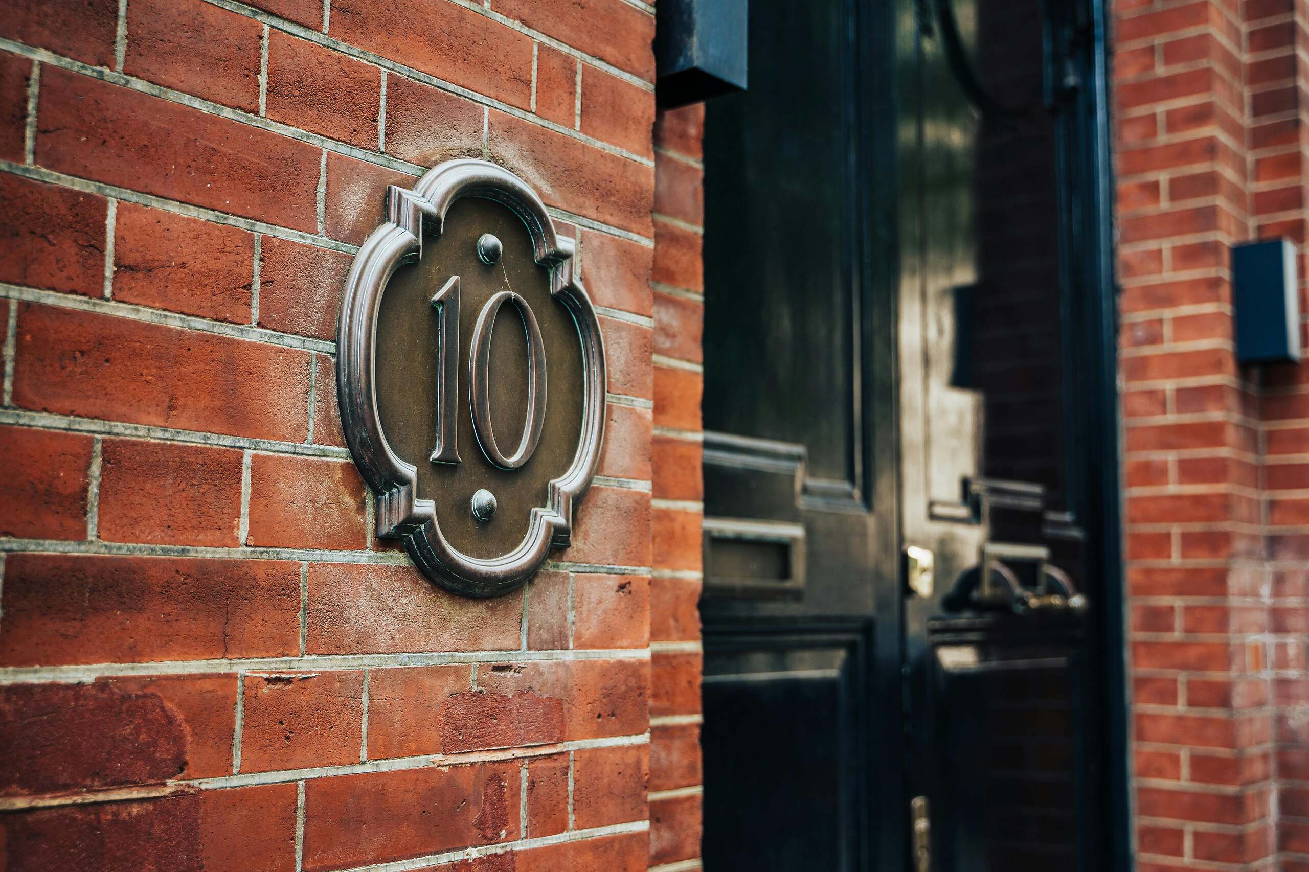 The tens in tarot. Image of a doorway with the address 10. The wall is brick.