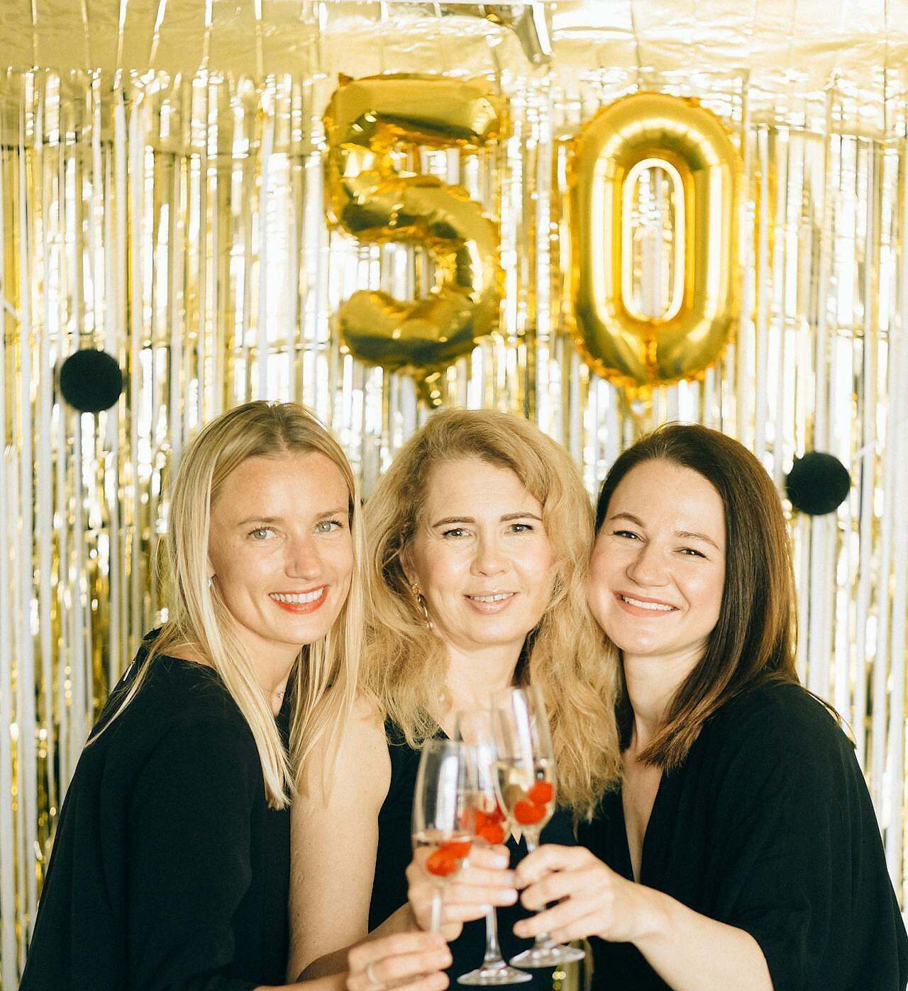 Redefining Beauty and Value After 50. Image of three women standing in front of a 50 balloon with champagne toasting.