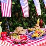 So this Memorial Day, as you dig into your favorite dishes and dodge those family debates, remember: the real flavor comes from kindness. Image of a picnic table full of food and drink with American flags hanging above.
