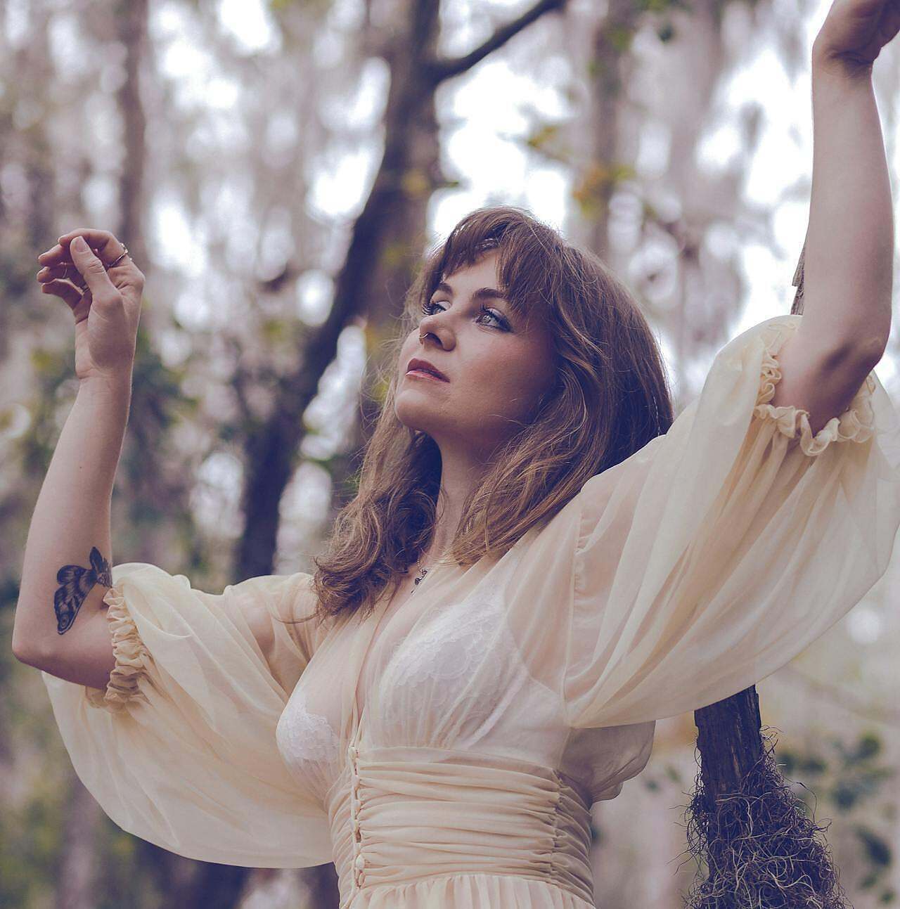 You Are Still Becoming. Image of a woman in a tree with a butterfly tattoo on her arm