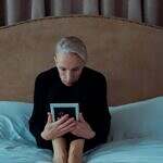 Image of a women sadly looking at a framed photo sitting on a large empty bed.
