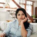 Pushing back doesn’t make you difficult. It makes you clear. Still, many of us were raised to be agreeable, accommodating, and quiet. Image of a woman looking into the camera sternly. She is seated on a white couch with a staircase and window behind her.