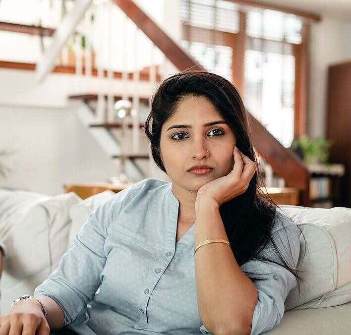 Pushing back doesn’t make you difficult. It makes you clear. Still, many of us were raised to be agreeable, accommodating, and quiet. Image of a woman looking into the camera sternly. She is seated on a white couch with a staircase and window behind her.