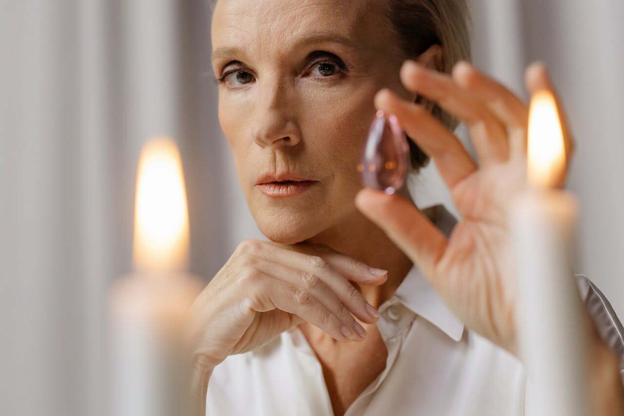Spiritual Development: A Sacred Conversation, Not a Checklist. Image of a woman sitting in front of two white taper candles that are lit holding a clear crystal.