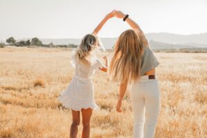 image of two woman in a field bathed with sunshine frolicking together in a joyous dance.