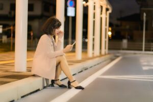 Image of a woman sitting looking at her phone longingly.