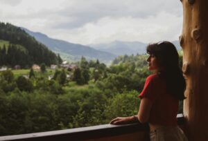Image of a woman standing on a wooden deck looking out to mountains.