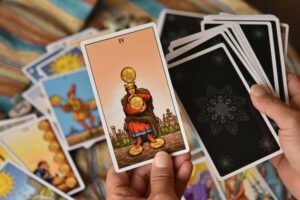 Image of hands with a pile of tarot cups with the 4 of pentacles prominent.