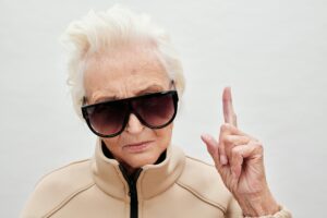 Image of an older woman wearing dark sunglasses pointing upwards.