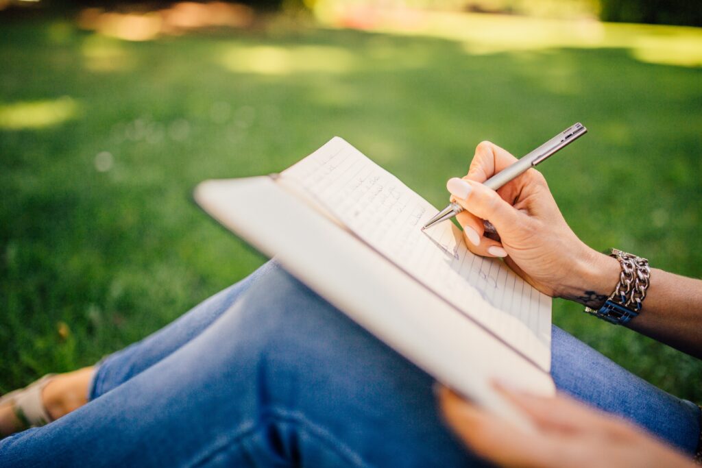 Image of a woman writing in a journal in the park.
