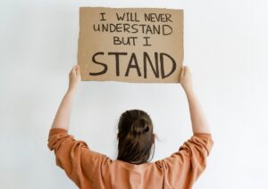 Image of a woman holding a sign "I will never understand, but I stand"