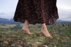 Image of a woman walking barefoot in grass with mountains behind her.