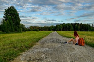 Image of a woman sitting on a long country road looking off into the distance.
