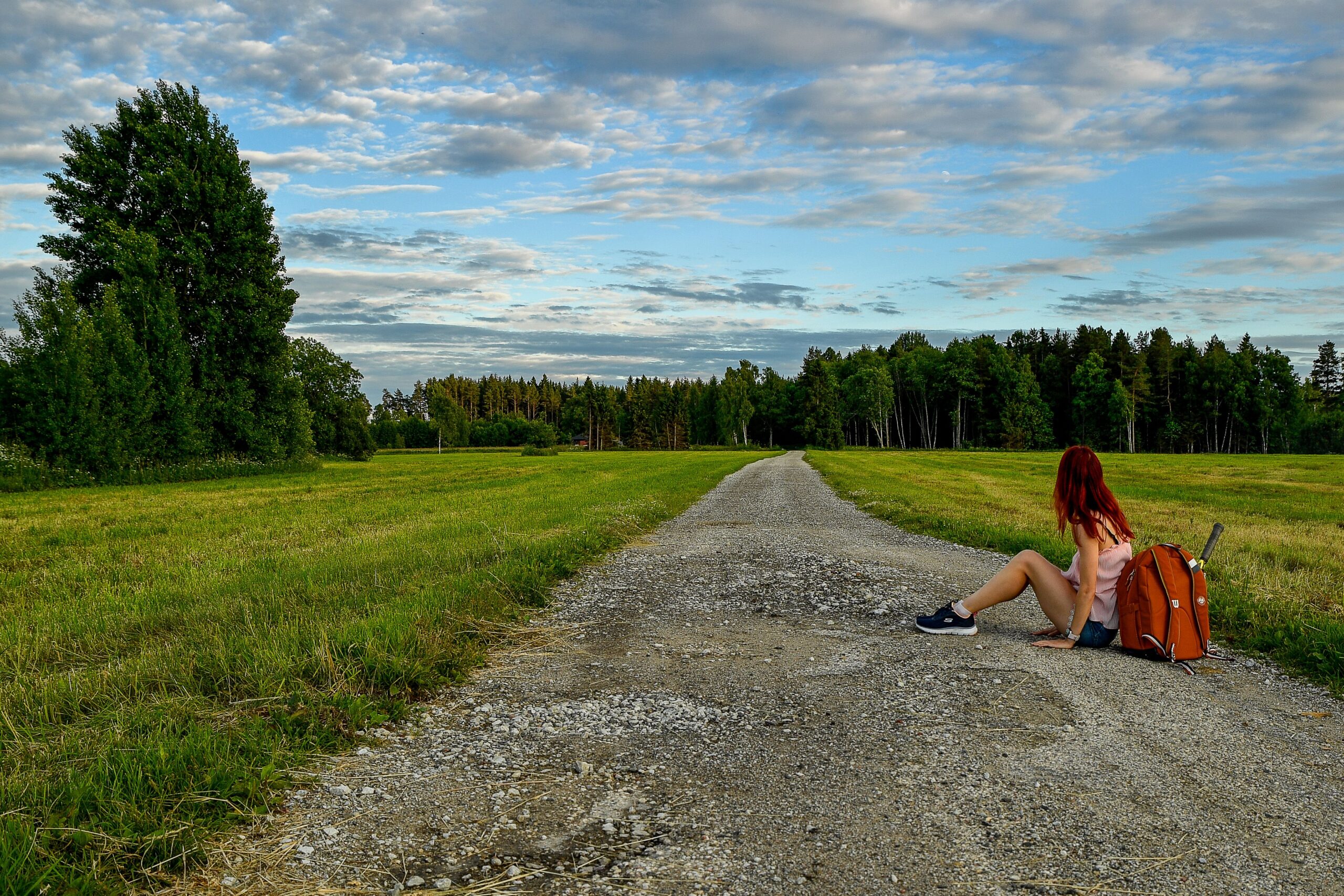 Image of a woman sitting on a long country road looking off into the distance.