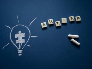 Image of the word Autism written in blocks with chalk and a drawn lightbulb with the puzzle piece.