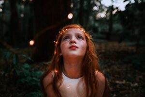 Image of a young girl in a wooded area with wisps of light surrounding her head.