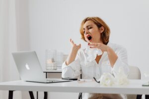 Image of a clearly exhausted woman at a laptop with piles of papers