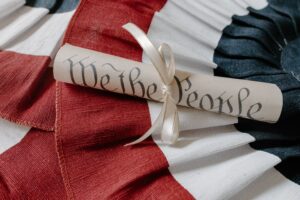 image of a scroll of paper with the words we the people written on it, sitting on red white and blue bunting.