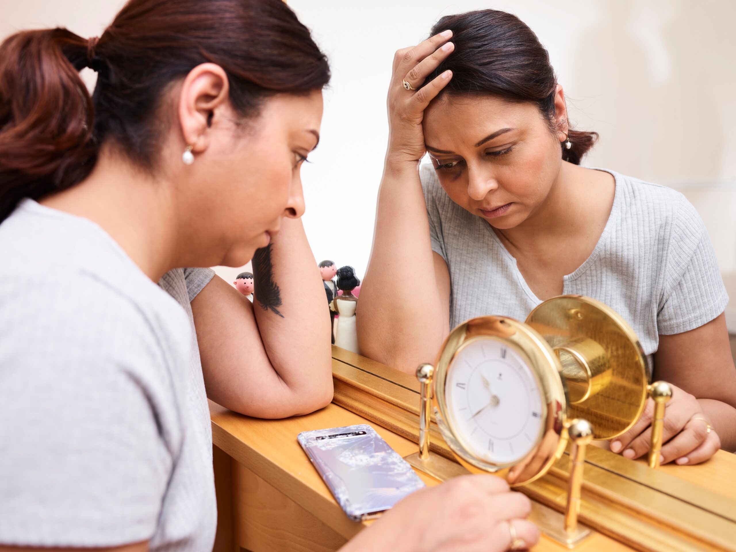 Image of a stressed out woman in front of a mirror and looking at a clock.