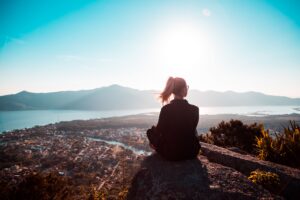 Image of a woman sitting on a high elevation looking down on a lake and mountains beyond.