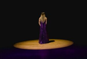 Image of a woman standing in a spotlight wearing a purple gown.