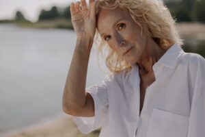 Image of a woman "cool heads prevail" outdoors on a warm day wiping her head with a body of water behind her.